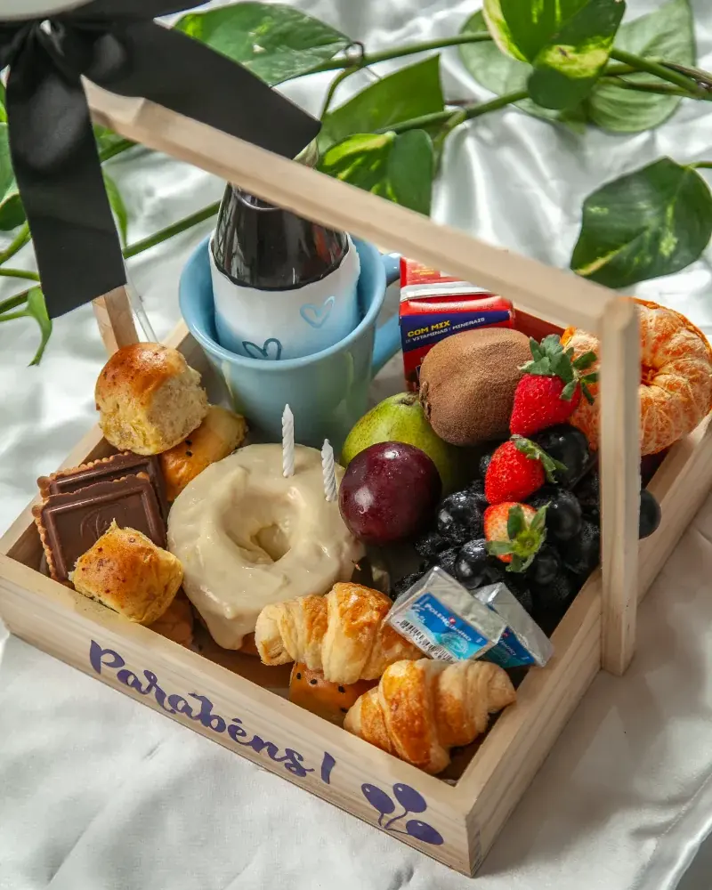 Cesta Happy Birthday Celebration em madeira com alça, caneca azul, rosca com vela, frutas e croissants