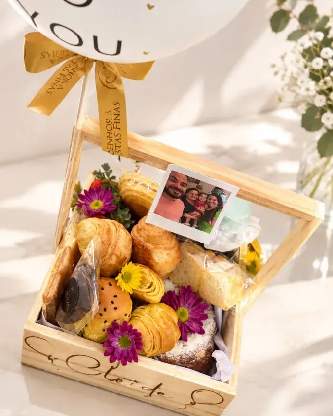 Cesta Happy Birthday Petit em caixa de madeira com croissants, flores e polaroide, com balão branco amarrado por laço dourado