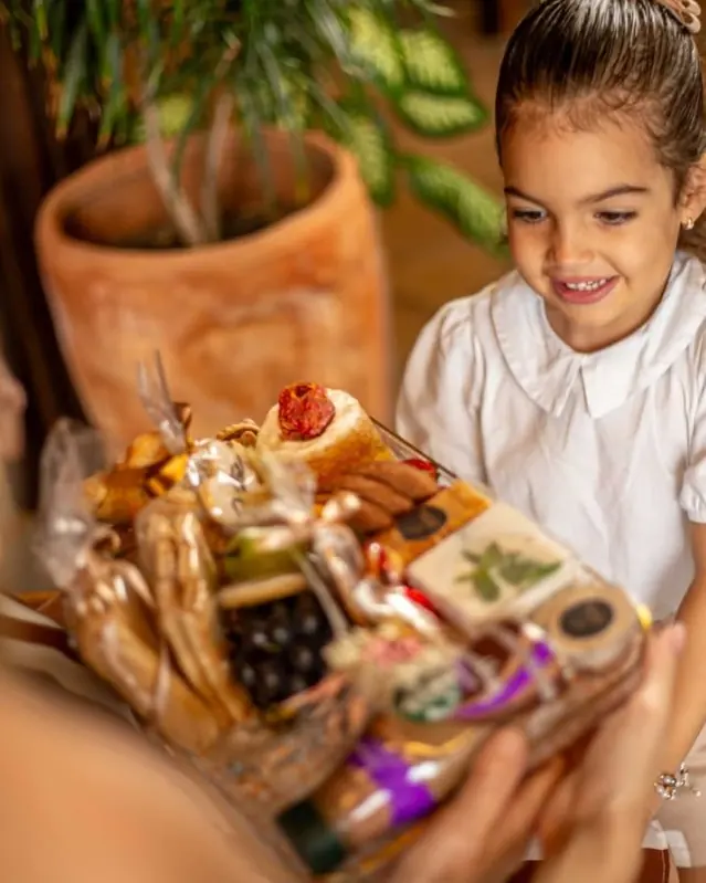 Menina sorrindo ao receber uma cesta com pães, frutas e biscoitos