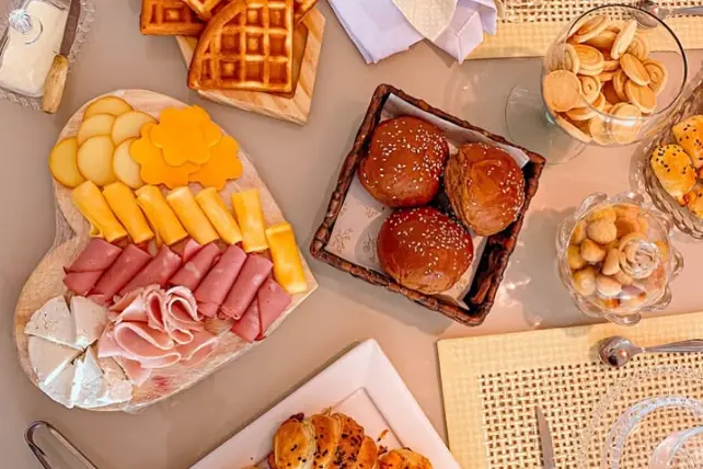 Mesa de café da manhã vista de cima, com waffles, croissants, pães, frios, queijos e biscoitos