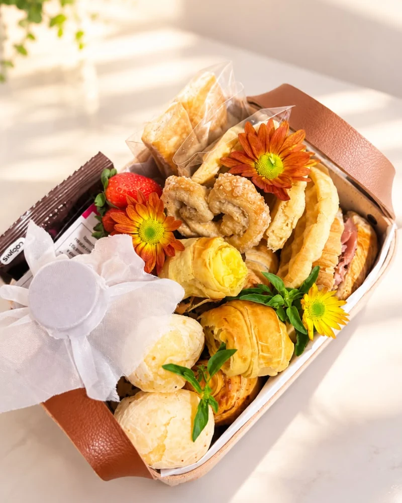 Cesta retangular em madeira com alças de couro, garrafa de suco de uva, morangos, uvas, biscoitos finos , sobre tecido de juta.